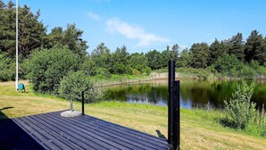 A wooden deck with a pond and trees in the background. - 4 Person Holiday Home in Laeso (Læsø)