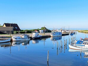 A calm harbor with several boats docked, a building with a sloped roof, and a clear sky. - 4 Star Holiday Home in Dannemare (Dannemare)