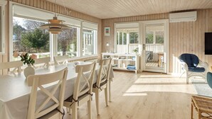 A spacious room with a wooden ceiling, large windows, a dining area with white furniture, and a seating area with a blue chair. - 4 Star Holiday Home in Dannemare (Dannemare)