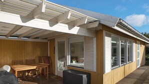 A covered outdoor area with a wooden deck, a table, chairs, and a grill. - 4 Star Holiday Home in Dannemare (Dannemare)