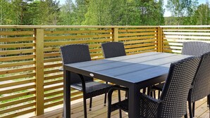 Une terrasse extérieure avec une table et des chaises, entourée d’une clôture en bois et d’arbres.