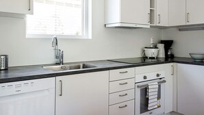 Une cuisine moderne avec des meubles blancs, un évier en acier inoxydable, une fenêtre et un four encastré.