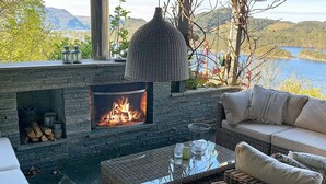 A cozy outdoor seating area with a stone fireplace, wicker furniture, and a view of a lake. - 7 Person Holiday Home in Jelsa (Suldal)