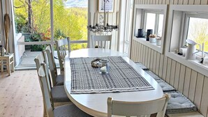 A dining area with a round table, white chairs, and a view of a garden through a large window. - 7 Person Holiday Home in Jelsa (Suldal)