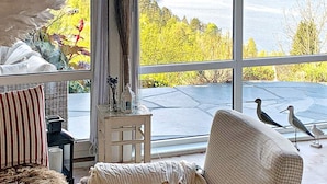 A cozy living room with a large window, a cushioned chair, a small table with a lantern, and a decorative plant. - 7 Person Holiday Home in Jelsa (Suldal)