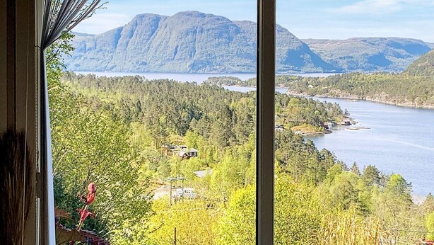 A view from a window overlooking a lake surrounded by dense forest and mountains. - 7 Person Holiday Home in Jelsa (Suldal)