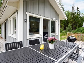 A deck with a table and chairs, a grill, and a house with a sliding door. - 4 Person Holiday Home in Bralanda (Bralanda)