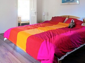 Una cama con una colcha multicolora, una mesita de noche con una lámpara y un cuadro en la pared.