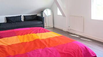 A bedroom with a bed, a dark sofa, a window, and a radiator.