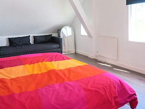A bedroom with a bed, a dark sofa, a window, and a radiator.
