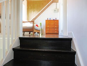 Una escalera conduce a un dormitorio con una cama, un aparador y un techo de madera.