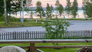 A view from a deck overlooking a road with a wooden fence, trees, and a body of water in the background.