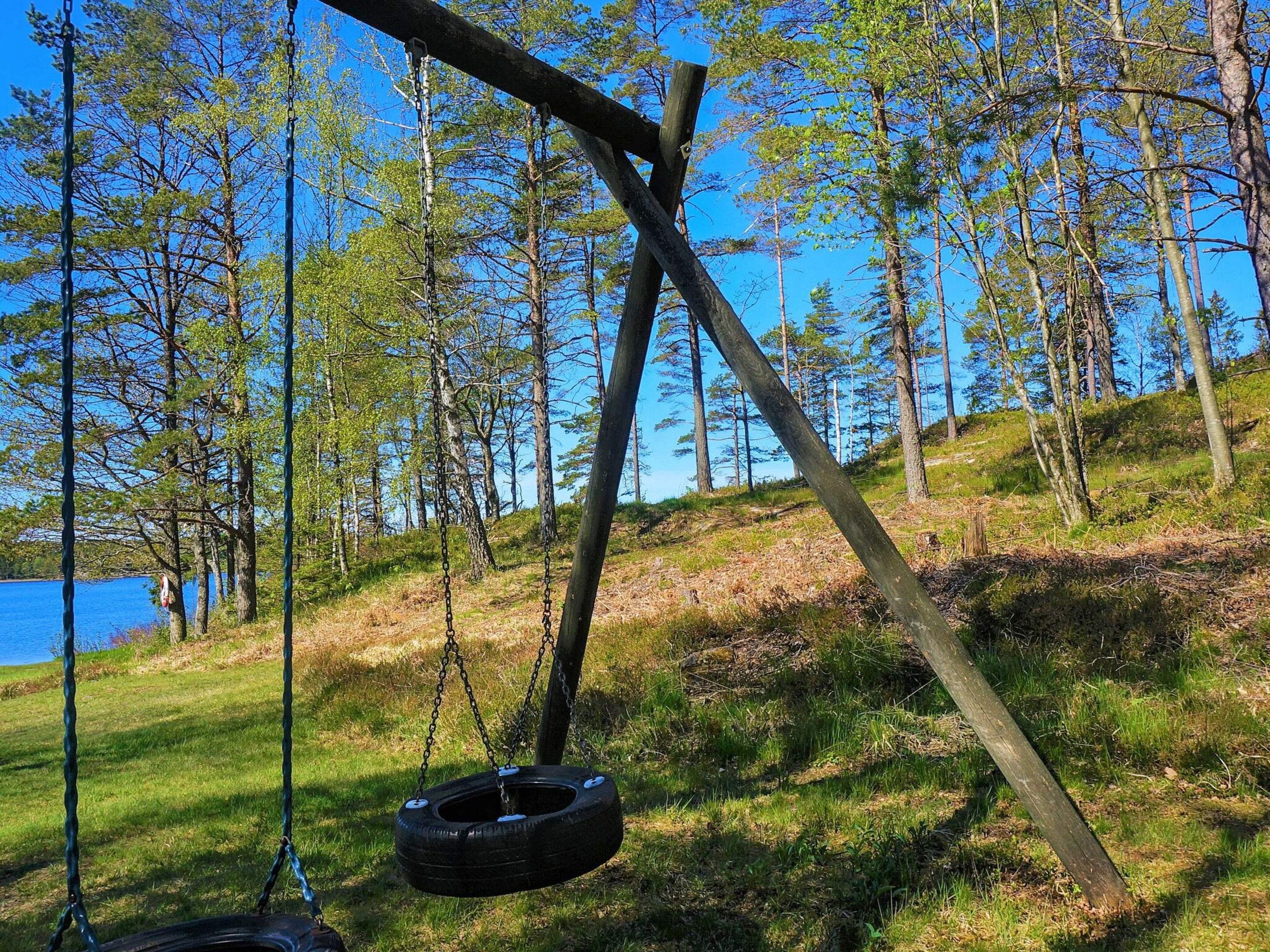 A tire swing suspended from a wooden structure in a wooded area with a body of water in the background.