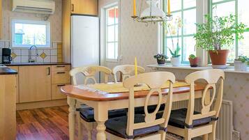 A kitchen with a dining table, chairs, a refrigerator, and a window with plants.