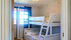Une chambre avec un lit superposé, une fenêtre, un radiateur et un tapis à rayures.