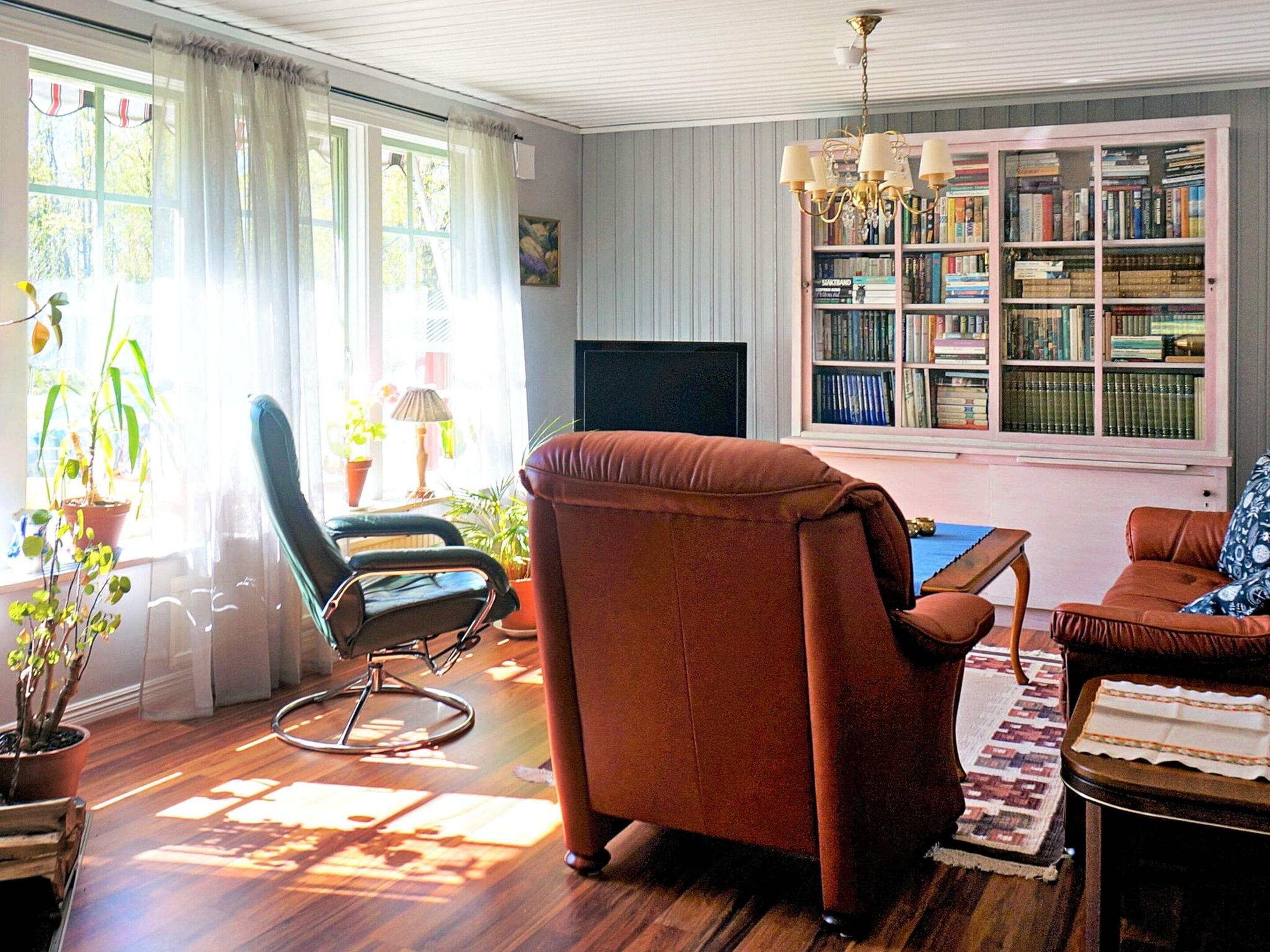 A living room with a brown leather armchair, a black office chair, a sofa, a television, and a bookshelf filled with books.