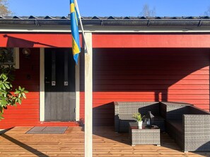 A red building with a flag, a door, and outdoor wicker furniture. - 4 Person Holiday Home in Fargelanda (Färgelanda)