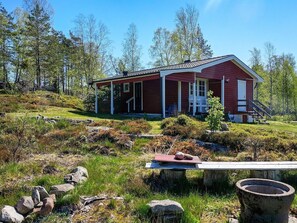 A red wooden cabin with a porch, surrounded by a natural landscape with rocks and trees. - 4 Person Holiday Home in Fargelanda (Färgelanda)