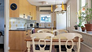 Une cuisine avec des meubles de rangement en bois, une table à manger avec des chaises, une horloge et une fenêtre ornée de plantes.