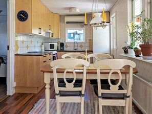 A kitchen with wooden cabinets, a dining table with chairs, a clock, and a window with plants. - 4 Person Holiday Home in Fargelanda (Färgelanda)
