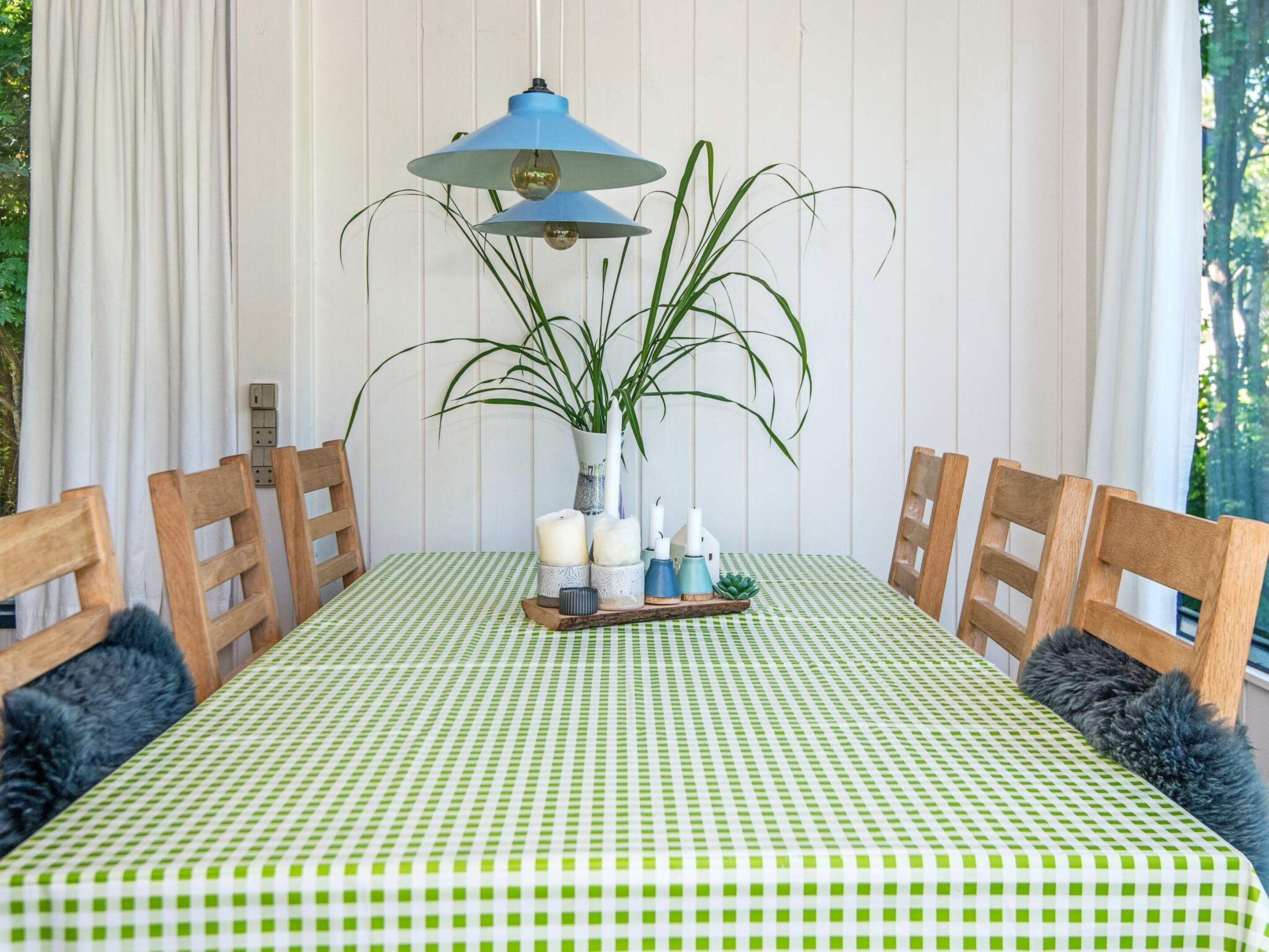 Una mesa de comedor con mantel a cuadros, rodeada de sillas de madera con cojines oscuros.