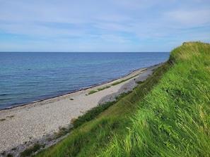 Un sentier cĂŽtier bordĂ© dâune plage de galets, de dunes herbeuses et de la mer.