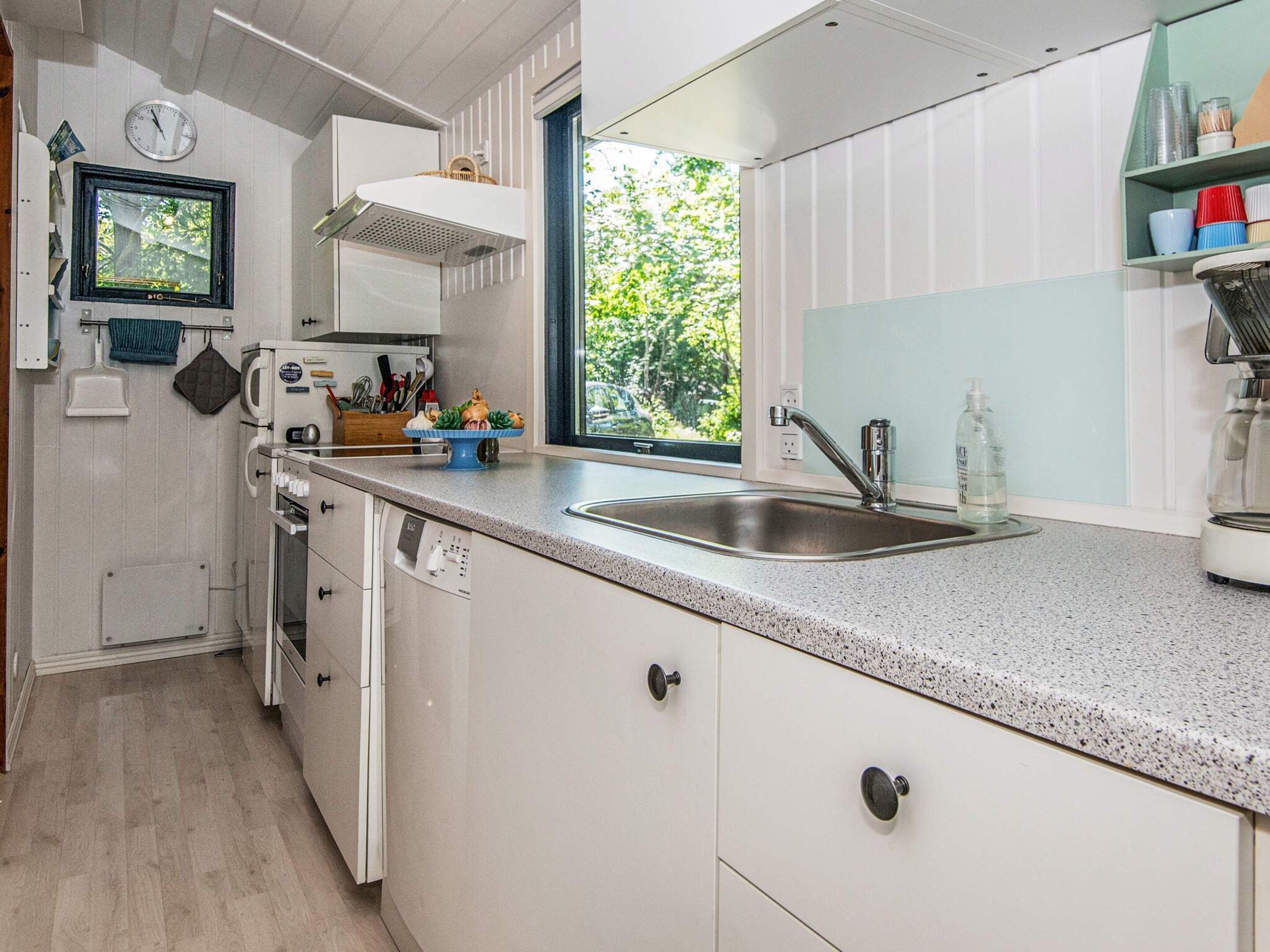 Una cocina moderna con pileta de acero inoxidable, muebles blancos y una ventana que ofrece vistas a la vegetación.