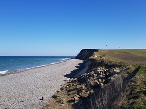 A pebbled beach with a rocky cliff and a clear blue sky. - 5 Person Holiday Home in Grenaa (Grenaa)