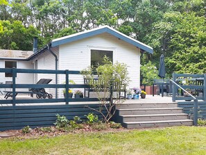 A small white building with a gabled roof, a wooden deck with chairs, and a staircase leading to the entrance. - 5 Person Holiday Home in Grenaa (Grenaa)