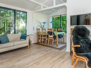 A room with a sofa, dining table with chairs, a TV, and a large window with curtains. - 5 Person Holiday Home in Grenaa (Grenaa)
