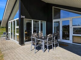 Un edificio moderno con el número 246, un patio con mesa y sillas, y una puerta de cristal que da al interior.