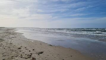 Una playa con olas, cielo despejado y tierra a lo lejos.