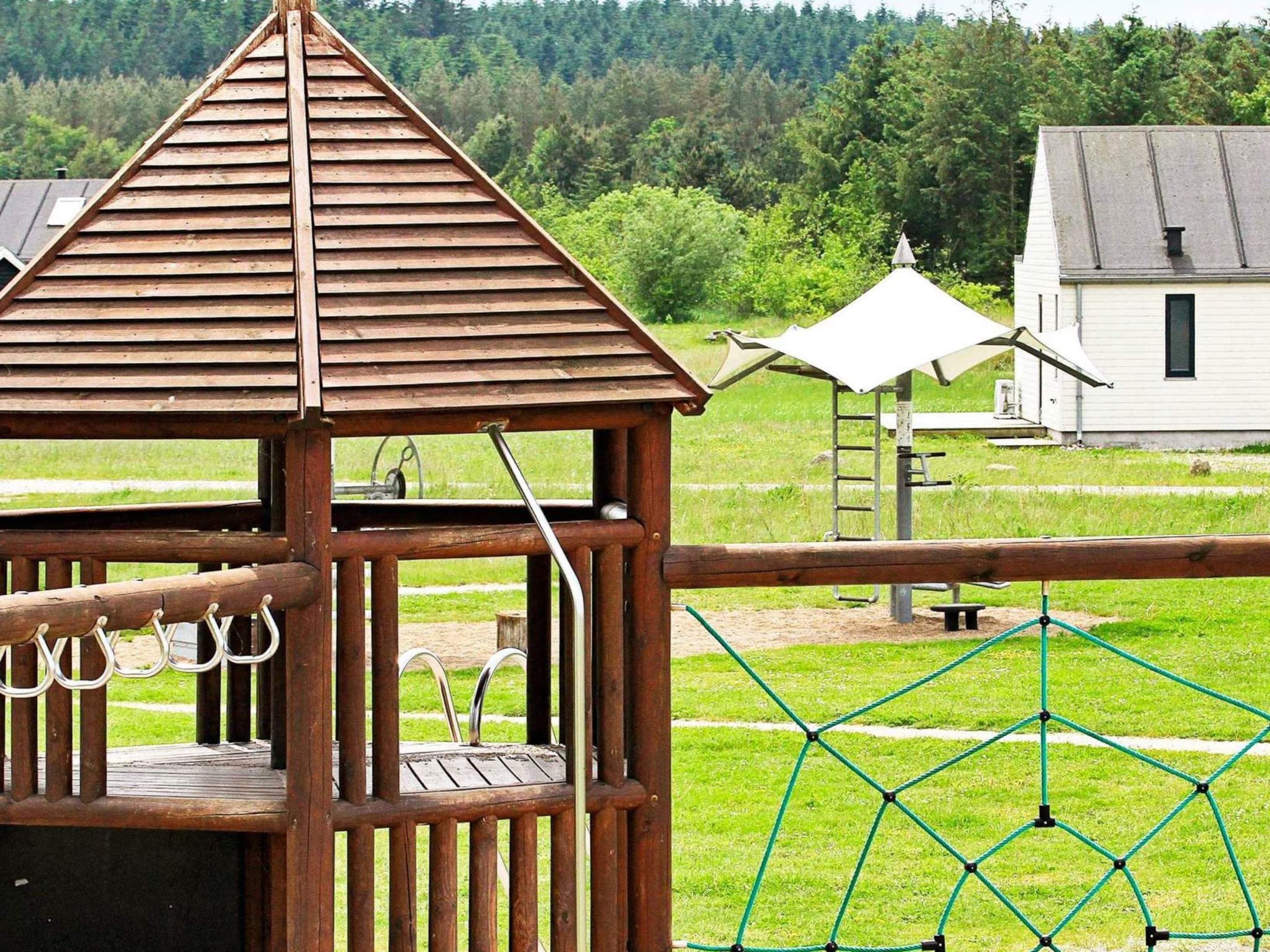 Une structure de jeu en bois, dotée d’un toit, d’une balançoire à corde et d’un filet d’escalade.