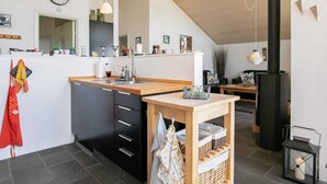 Eine moderne Küche mit einer zentralen Kochinsel, schwarzen Schränken und einer Holz Arbeitsplatte. Spüle, Herd und diverse Küchenutensilien befinden sich auf der Arbeitsfläche.