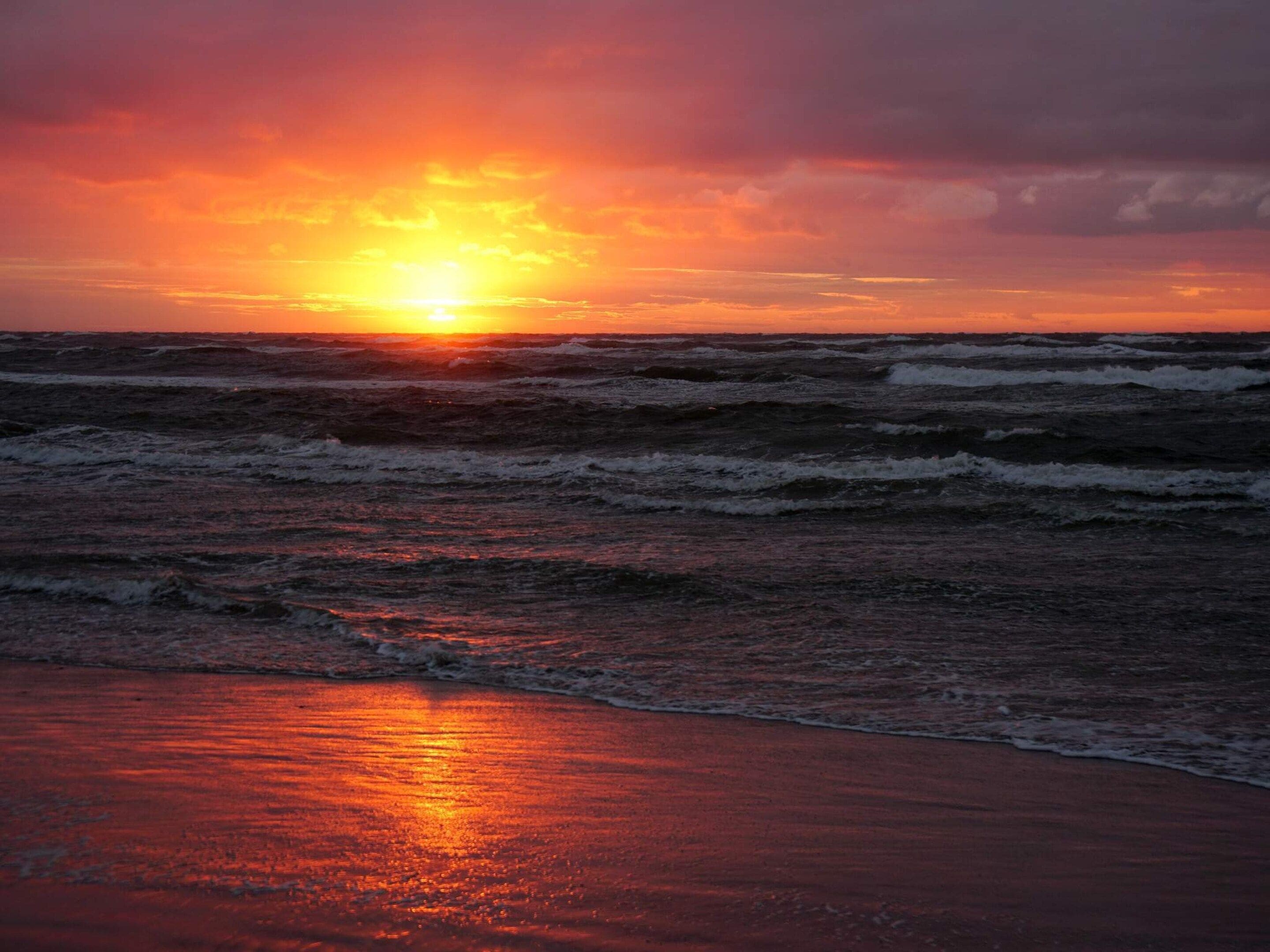 A sunset over the ocean with waves approaching the shore.