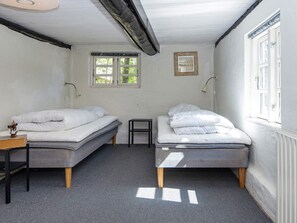 A room with two single beds, a small table, a lamp, and a window with a view of greenery. - 7 Person Holiday Home in Grenaa (Grenaa)