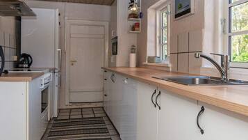 Una cocina compacta con alacenas blancas, encimera de madera, pileta de acero inoxidable y alfombra estampada.