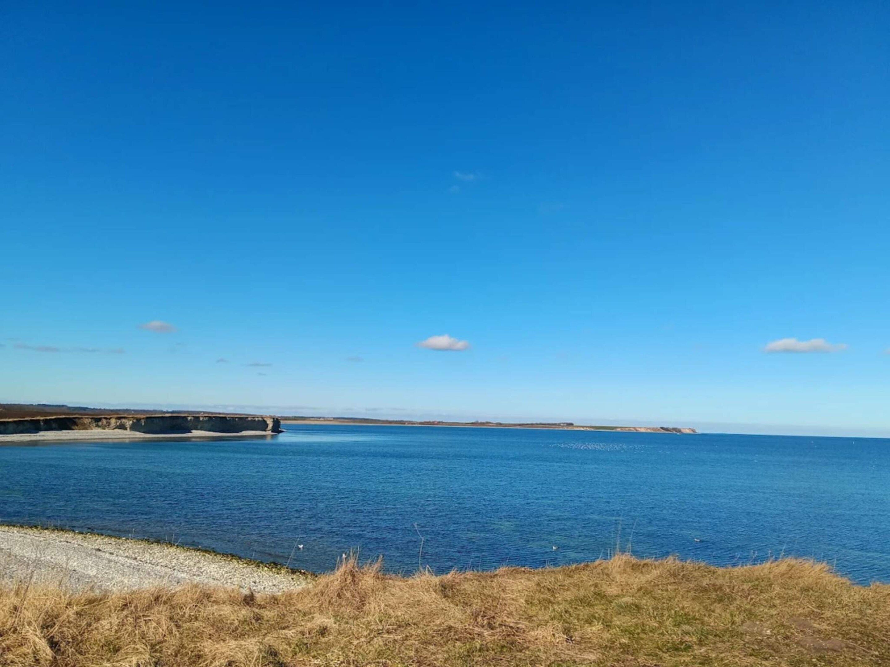 Eine Küstenlandschaft mit blauem Himmel, einem Gewässer und einer fernen Küstenlinie.