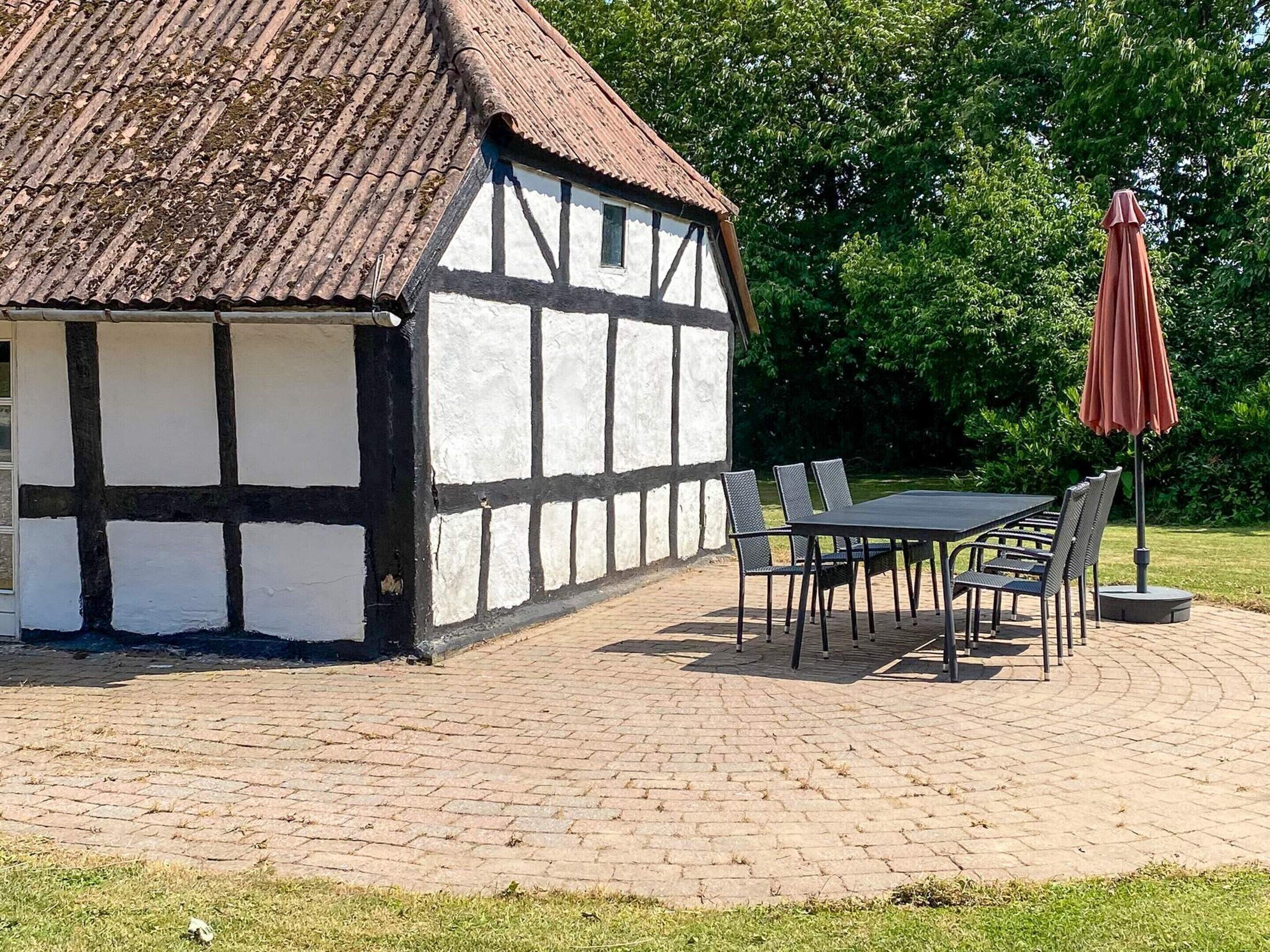 Un bâtiment traditionnel à colombages, doté d’un toit en tuiles, d’une terrasse pavée et d’une table entourée de chaises.