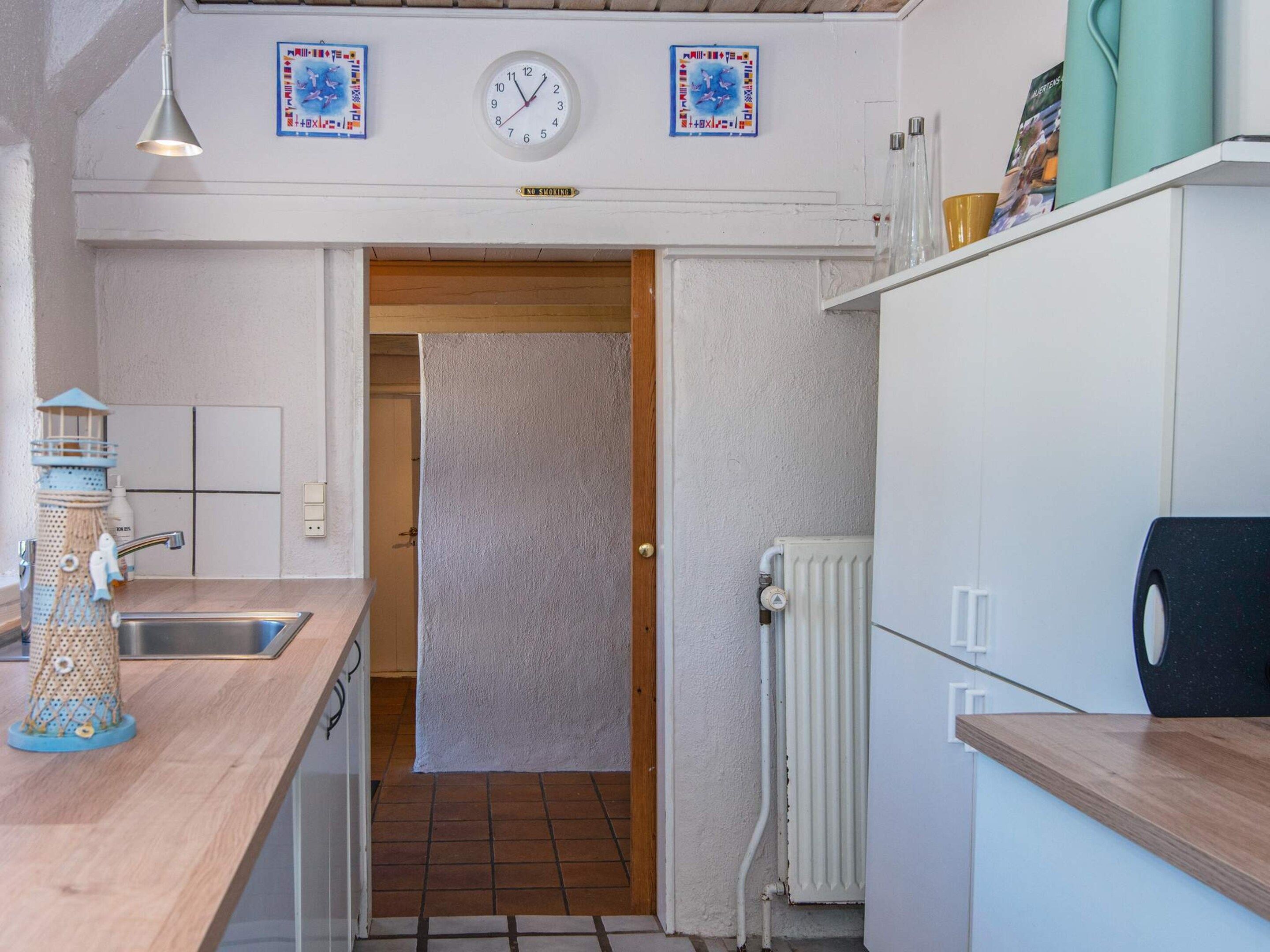 Et lille køkken med en træbordplade, en vask, et ur og en radiator.