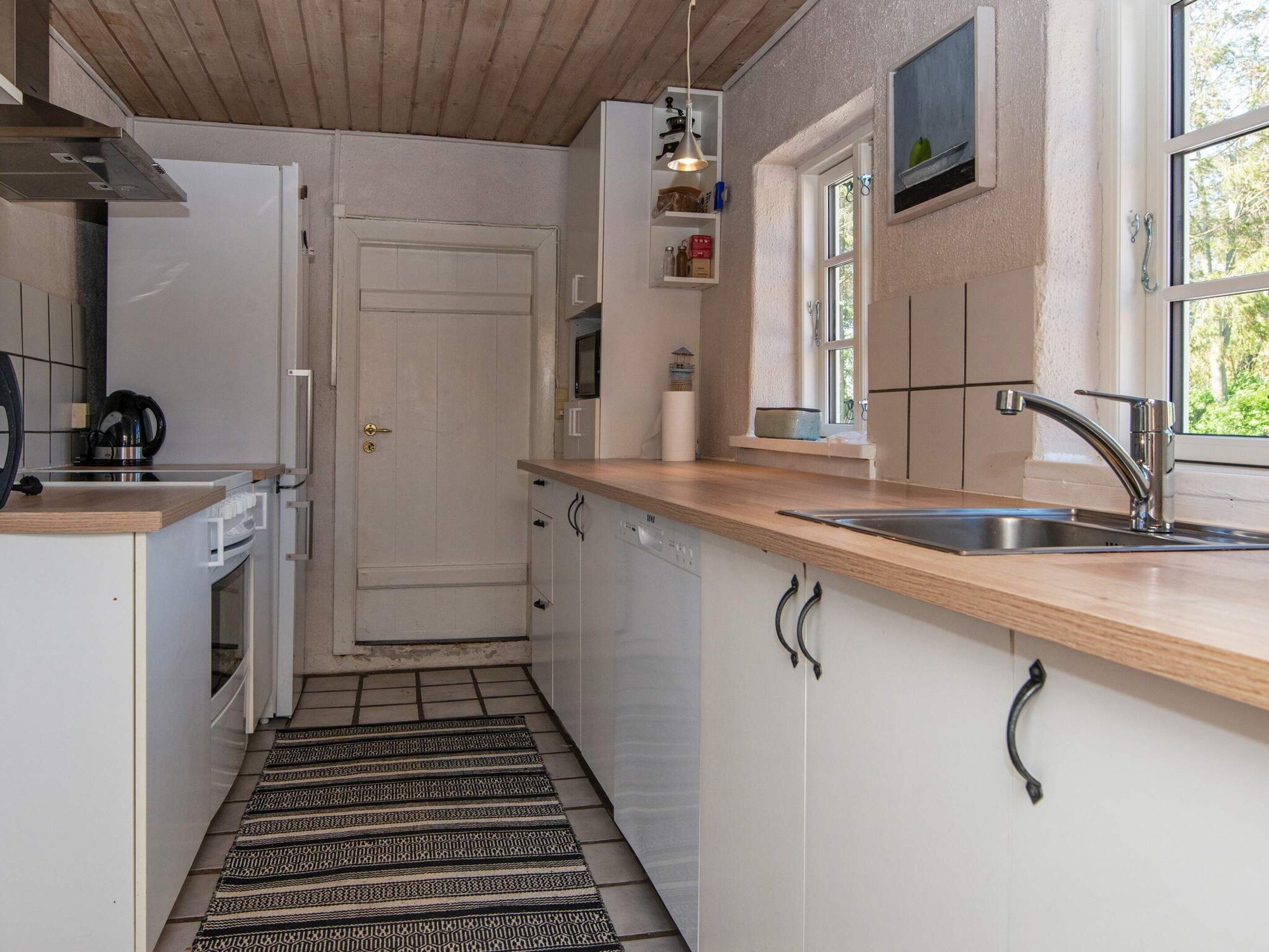 A compact kitchen with white cabinets, a wooden countertop, a stainless steel sink, and a patterned rug.