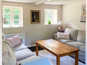 Uma sala de estar com um sofá, uma mesa de centro de madeira e duas janelas.