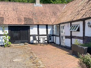 A traditional building with a tiled roof, a black and white exterior, and a brick pathway leading to a seating area with two chairs.