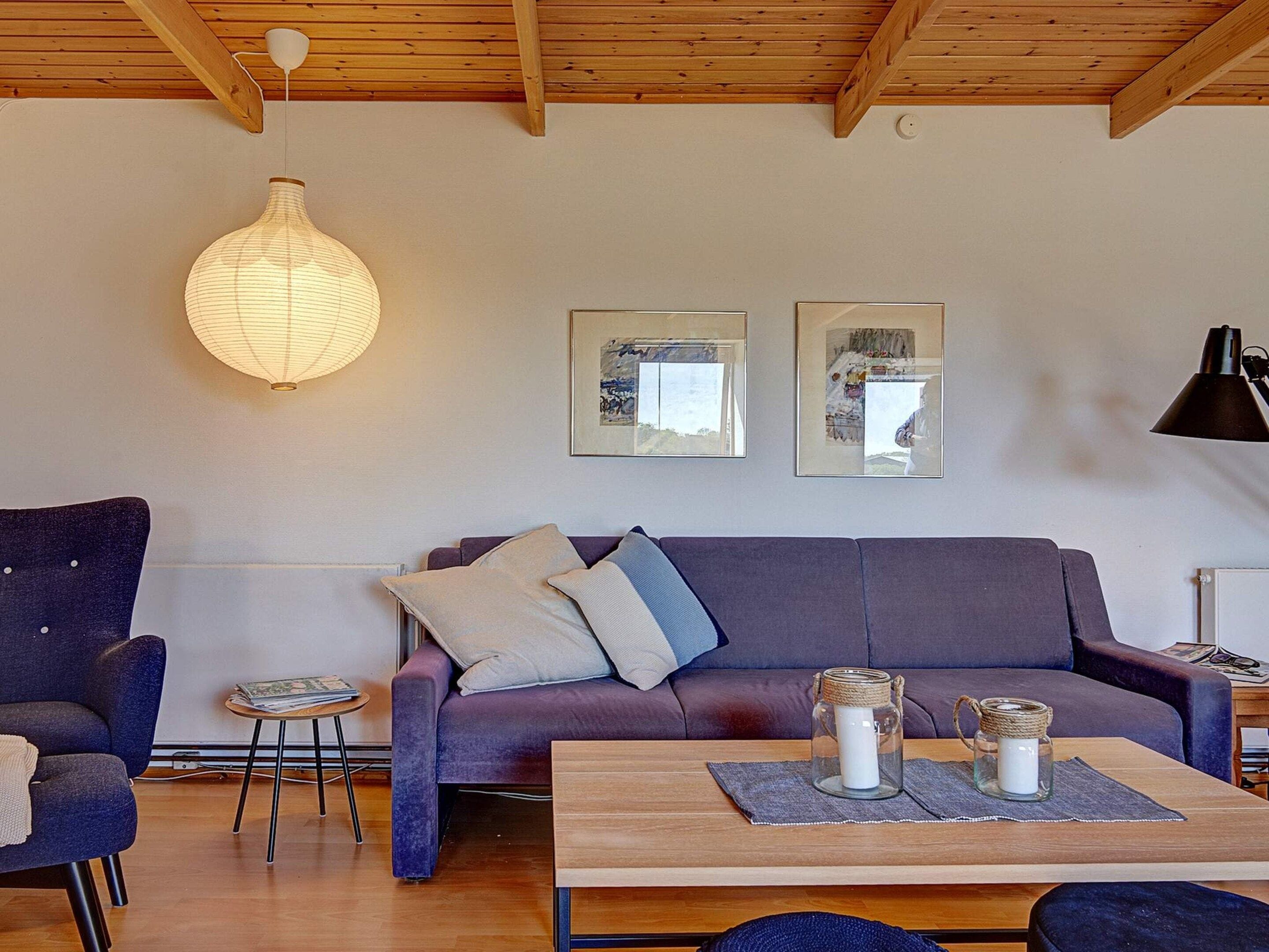 A modern living room with a wooden ceiling, a purple sofa, a round table, and a hanging light fixture.