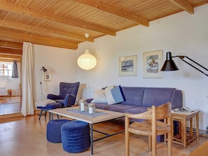 Een gezellige woonkamer met een houten plafond, een bank, een tafel en blauwe poefs.