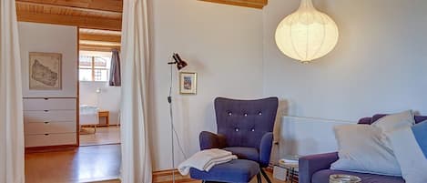 A cozy living room with a wooden ceiling, a blue armchair, a sofa, a table with candles, and a floor lamp.