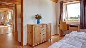 A room with wooden flooring, a bed, a desk with a chair, a wooden cabinet, and a window with curtains.