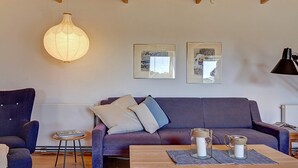 A modern living room with a wooden ceiling, a purple sofa, a blue armchair, and a wooden coffee table with decorative jars.