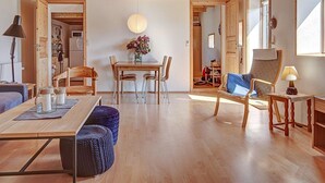 A spacious living area with a wooden ceiling, a dining table with chairs, a sofa, and a lounge chair.