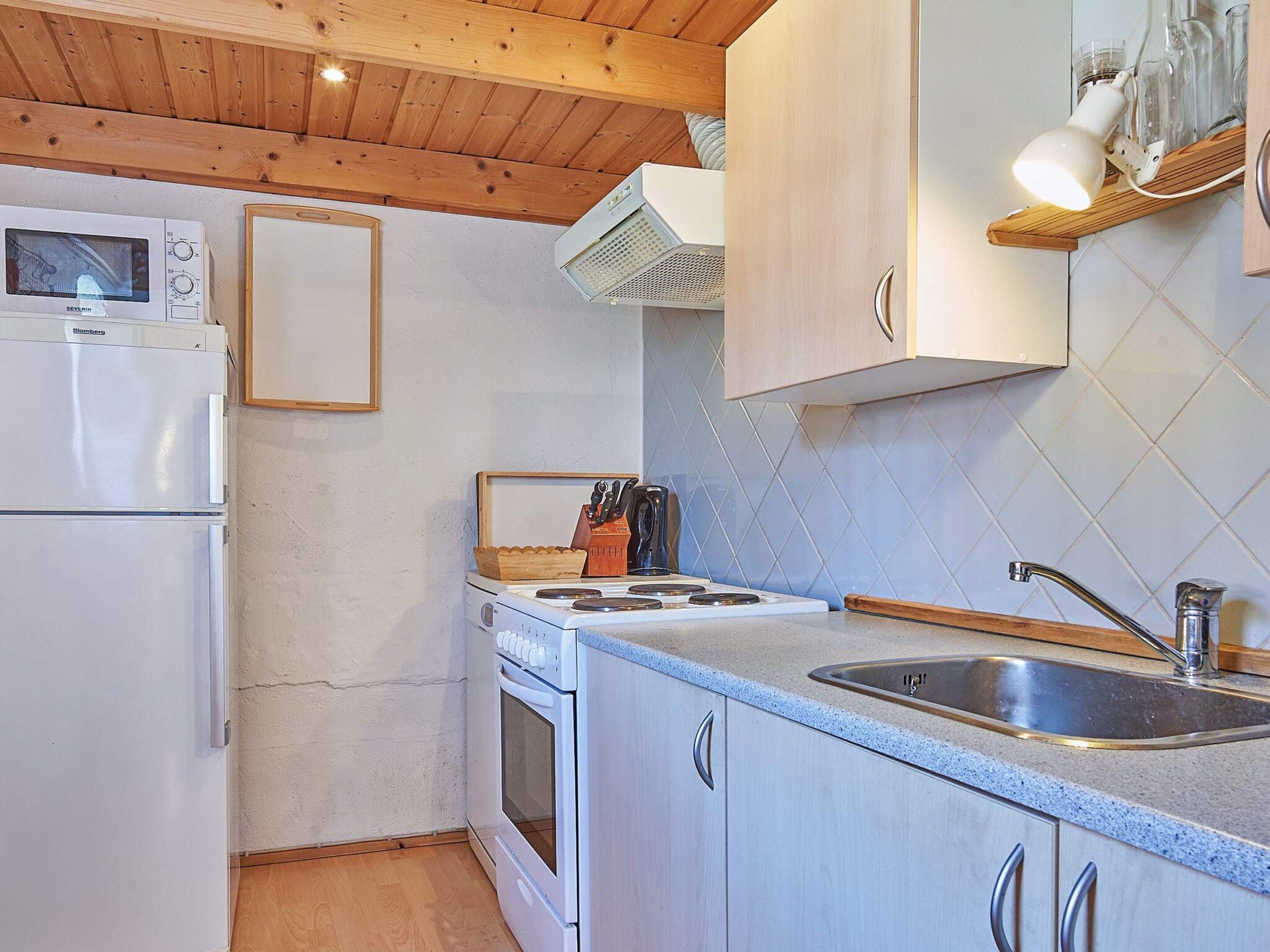 A compact kitchen with a microwave, stove, sink, and wooden cabinets.